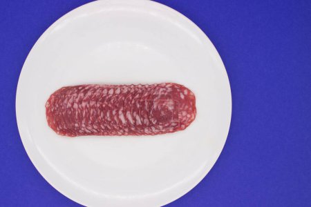 Salami tranché délicatement disposé sur une assiette blanche au-dessus du bleu