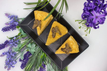 Three honey cake slices adorned with chocolate butterflies, surrounded by fresh flowers.