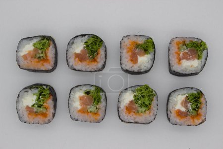 Eine Reihe Lachs-Sushi-Rollen mit knusprigem Salat, cremiger Avocado und leuchtend orangefarbenem Rogen, präsentiert vor einem weißen Hintergrund.