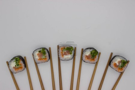 An overhead shot showcasing an inventive sushi presentation, where four pieces of sushi are arranged in a straight line, each flanked by a pair of bamboo chopsticks set against a clean white backdrop. The sushi rolls are meticulously crafted, featuri