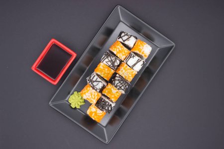 Dieses verlockende Bild zeigt eine Reihe kalifornischer Sushi-Rollen mit orangefarbenem Masago, die neben einem Klecks Wasabi und einem roten Gericht Sojasauce auf einem schlanken, schwarzen Tablett angeordnet sind..
