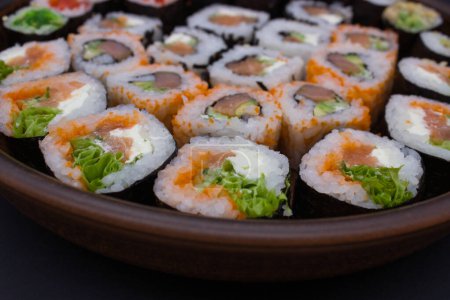 This image features a large circular wooden platter filled with an array of sushi rolls, perfectly arranged in a circular pattern. The assortment includes a selection of rolls with fresh fish, avocado, and crisp vegetables. A small red dish filled wi
