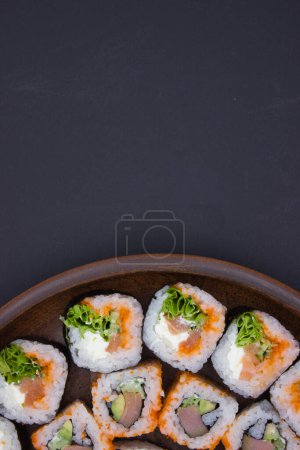 Das Foto zeigt ein kreatives Sushi-Arrangement, das die eine Seite einer runden Holzplatte einnimmt und den dunklen Hintergrund den Rest des Rahmens füllt. Diese exzentrische Komposition schafft einen fesselnden negativen Raum, der das Auge auf das det lenkt