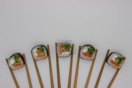 Nagłówek prezentujący nowatorską prezentację sushi, w której cztery kawałki sushi ułożone są w linii prostej, z których każdy otoczony jest parą bambusowych pałeczek ustawionych na czystym białym tle. Sushi bułki są starannie wykonane, featuri