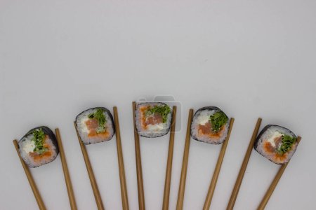 Une photo aérienne montrant une présentation inventive de sushis, où quatre morceaux de sushis sont disposés en ligne droite, chacun flanqué d'une paire de baguettes de bambou placées sur un fond blanc propre. Les rouleaux de sushi sont méticuleusement fabriqués, featuri