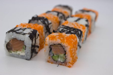 L'image présente un angle dynamique de rouleaux de sushi assortis en une formation décalée, soulignant le contraste entre les rouleaux californiens recouverts de masago et les simples sushis enveloppés d'algues. Le masago orange ajoute une texture brillante et caviar, whi