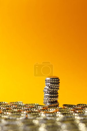 Column composed of bottle caps positioned downward protruding from the surface formed by many other caps positioned downward. Orange gradient background.