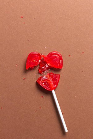 Piruleta roja en forma de corazón roto en varios pedazos sobre un fondo marrón. Concepto de rotura sentimental.