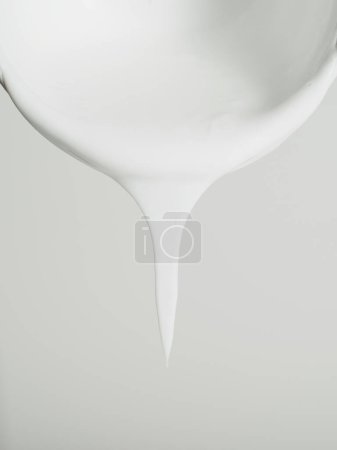 Photo for Image focusing on a thick drip of white paint about to drop from the smooth edge of a bowl. - Royalty Free Image
