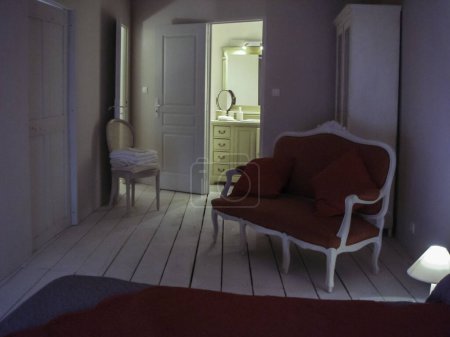 Téléchargez les photos : Chambre d'hôtes de style provençal dans des tons blanc crème avec salle de bains privative comprenant un banc, fauteuil, armoire et lit - en image libre de droit