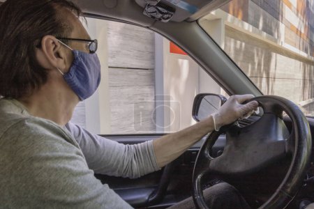 Téléchargez les photos : Homme conduisant sa voiture avec un masque et des gants chirurgicaux pour se protéger contre les maladies et les virus comme le coronavirus Covid-19 - en image libre de droit