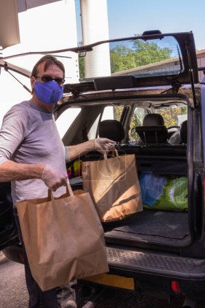 Téléchargez les photos : Homme magasinant dans un lecteur de supermarché avec un masque et des gants chirurgicaux pour se protéger contre les maladies et les virus comme le coronavirus Covid-19 pendant le confinement - en image libre de droit