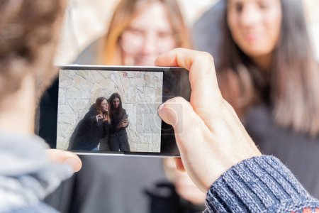 Téléchargez les photos : Jeune homme prenant en photo avec son smartphone ses 2 copines - femmes blondes et femmes brunes - multiraciales et multi-ethniques - en image libre de droit