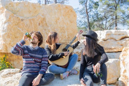 Téléchargez les photos : Les jeunes s'amusent à faire la fête avec un musicien qui joue de la guitare lors d'un pique-nique original dans une carrière de pierre - en image libre de droit