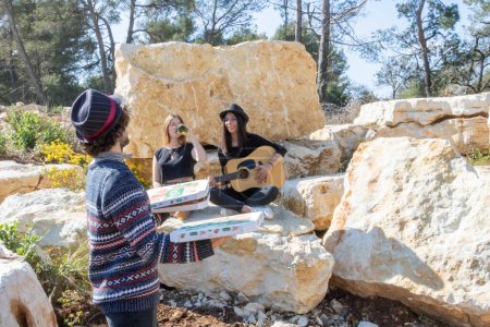 Téléchargez les photos : Les jeunes s'amusent à faire la fête avec un musicien qui joue de la guitare lors d'un pique-nique excentrique dans une carrière de pierre et se fait livrer une pizza - en image libre de droit