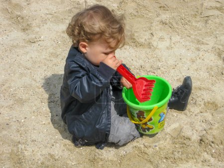 Téléchargez les photos : Enfant jouant dans le sable avec son seau et râteau - en image libre de droit