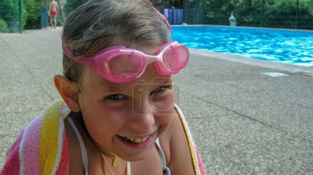 Téléchargez les photos : Jeune fille sortant de la piscine avec ses lunettes de plongée et serviette de bain sur elle - en image libre de droit