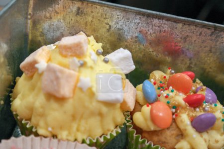 Foto de 2 Cupcakes decorados con diferentes caramelos de colores en una caja de lata - Imagen libre de derechos