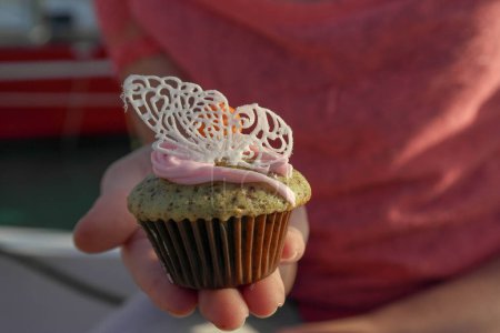 Téléchargez les photos : Main d'enfant offrant cupcake avec un papillon en dentelle de sucre, cupcake découpé - en image libre de droit