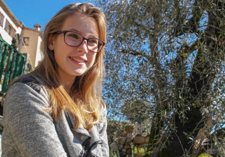 Photo for Young smiling blonde teenager with glasses in Provence in front of an olive tree in France - Royalty Free Image