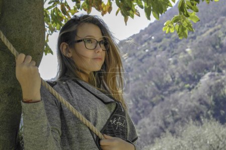 Téléchargez les photos : Jeune fille blonde avec des lunettes accrochées à une corde sous un oranger en Provence à Bar sur Loup, capitale de l'oranger - en image libre de droit
