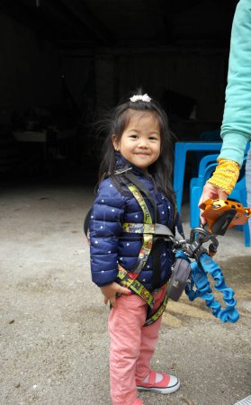 Photo for Child, little Eurasian girl mixed Chinese and French, looking at the camera, with her equipment for tree climbing - Royalty Free Image