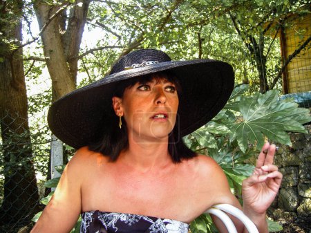 Photo for Woman with a hat hat, in profile at a garden party, smoking cigar - Royalty Free Image