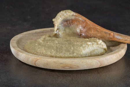 Téléchargez les photos : Anchoade, purée d'anchois à la crème, dans une assiette en bois avec une cuillère en bois d'olivier sur fond sombre gros plan. Cuisine Méditerranéenne pour Trempettes - en image libre de droit