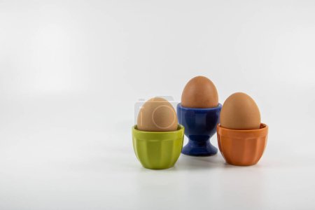 Photo for Eggs to the whole shell egg cups in different colors green blue and orange on white background studio - Royalty Free Image