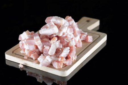 Pork bacon cut and placed on a wooden cutting board on a black background with reflection.