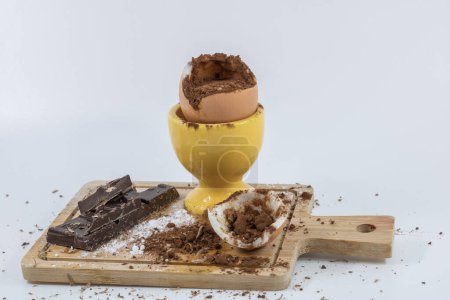 Gekochtes Ei zum süßen Dessert Rezept mit Schokoladenpuder auf Holzbrett und gelbem Eierbecher