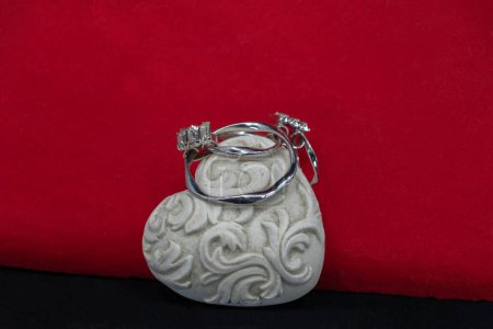 Joya de plata con diamantes presentada sobre un corazón de cerámica blanca sobre fondo rojo y negro