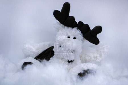 Téléchargez les photos : Saison d'hiver avec un cerf blanc en peluche et des bois dans un fond neigeux, et une écharpe pour garder au chaud, fin d'année festive et Nouvel An - en image libre de droit