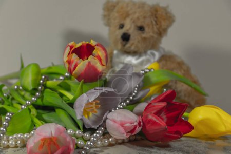 Téléchargez les photos : Printemps arrivée du printemps avec les premières tulipes entourées d'un collier de perles et un ours en peluche en arrière-plan chambre féminine - en image libre de droit