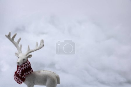 Téléchargez les photos : Cerf blanc avec un foulard aux couleurs de Noël dans une neige de décoration blanche pour les fêtes de Noël, le Nouvel An et la saison d'hiver - en image libre de droit
