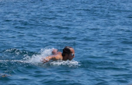 Mann schwimmt Schmetterling schwimmen im offenen Meer, Kopf aus dem Wasser, um Luft zu holen