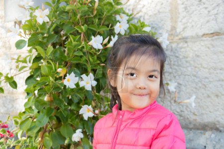 Photo for Chinese and French Eurasian Little Girl Smiling Very Smiling in Front of a Blossoming Grove - Portrait - Royalty Free Image