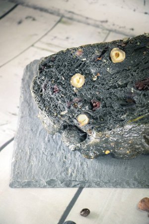 Téléchargez les photos : Gros plan sur un pain noir à base de charbon et de fruits secs sur un plat d'ardoise - en image libre de droit