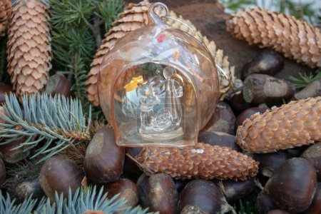 Pequeño belén de Navidad en una bola de Navidad rodeada de conos de pino y castañas