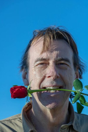 Man holding a red rose between his teeth to play young first