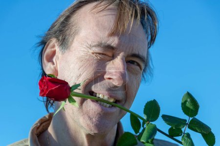 Photo for Man holding a red rose between his teeth to play young first - Royalty Free Image