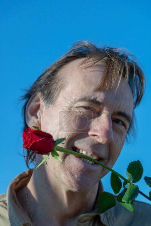 Man holding a red rose between his teeth to play young first
