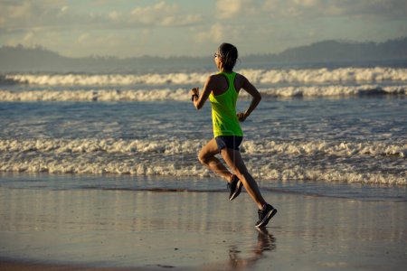 Foto de Estilo de vida saludable joven fitness mujer corriendo en la playa del amanecer - Imagen libre de derechos