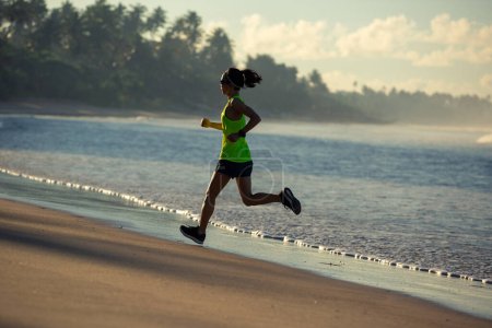 Foto de Estilo de vida saludable joven fitness mujer corriendo en la playa del amanecer - Imagen libre de derechos