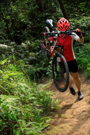 Téléchargez les photos : Femme cycliste porter un vélo de montagne marche sur le sentier de la forêt tropicale - en image libre de droit