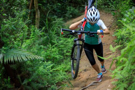 Foto de Mujer ciclista llevar una bicicleta de montaña caminando por sendero bosque tropical - Imagen libre de derechos