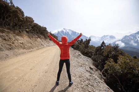 Foto de Mujer trail runner brazos abiertos a las montañas cubiertas de nieve - Imagen libre de derechos