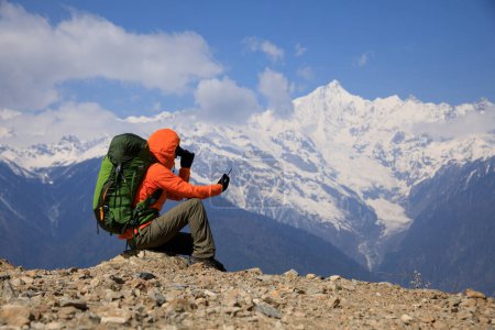 Photo for Woman backpacker taking photo of  high altitude mountains with smart phone - Royalty Free Image