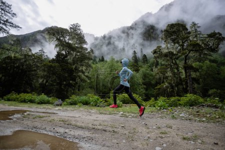 Foto de Mujer trail runner cross country running in high altitude mountain forest - Imagen libre de derechos