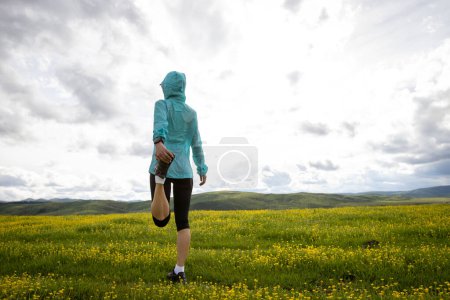 Foto de Corredor de sendero de mujer estirando piernas en flores en montaña de pastizales de gran altitud - Imagen libre de derechos